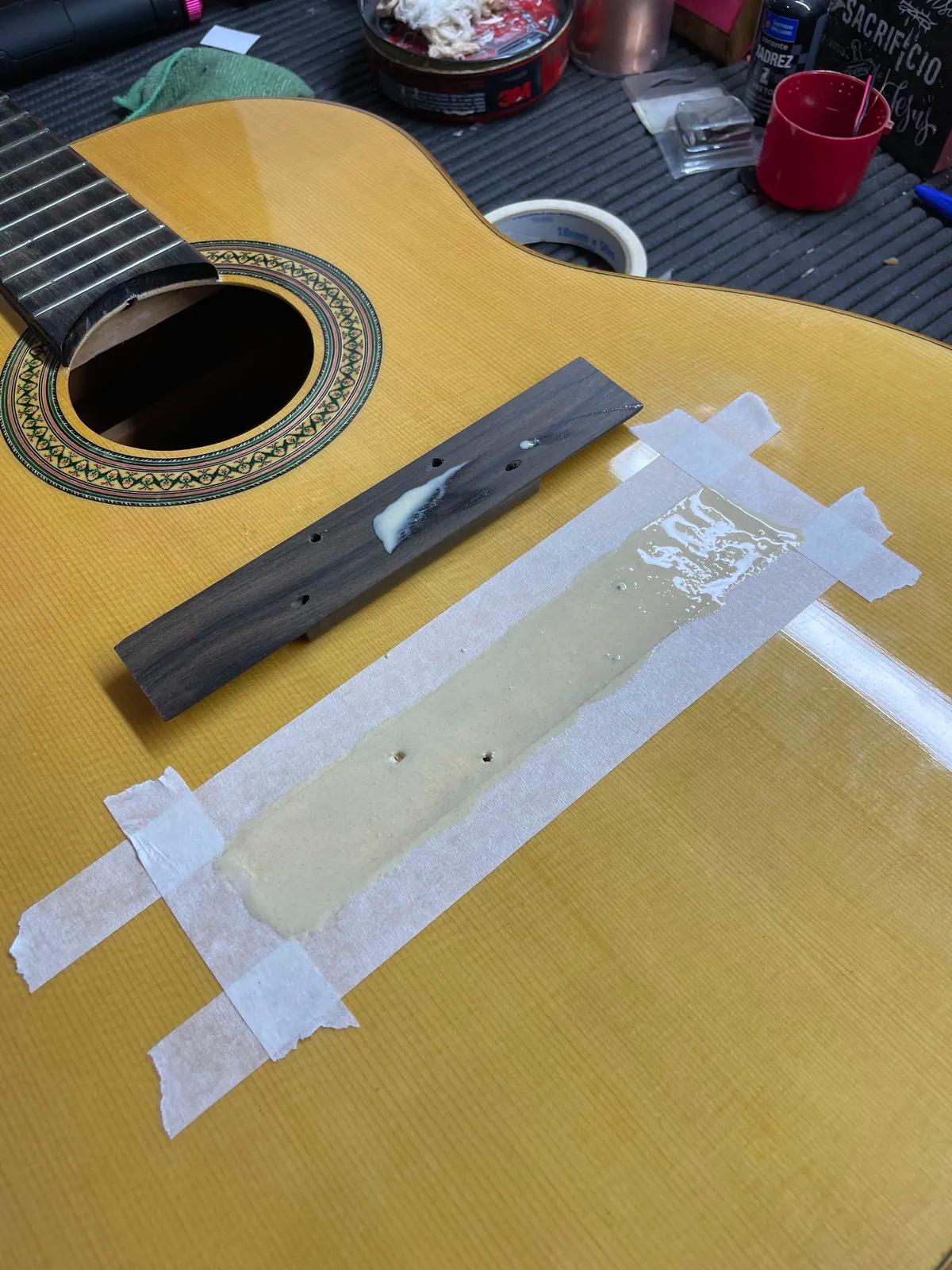 Colagem de cavalete de violão clássico: área demarcada com fita e cavalete novo com cola sobre o tampo