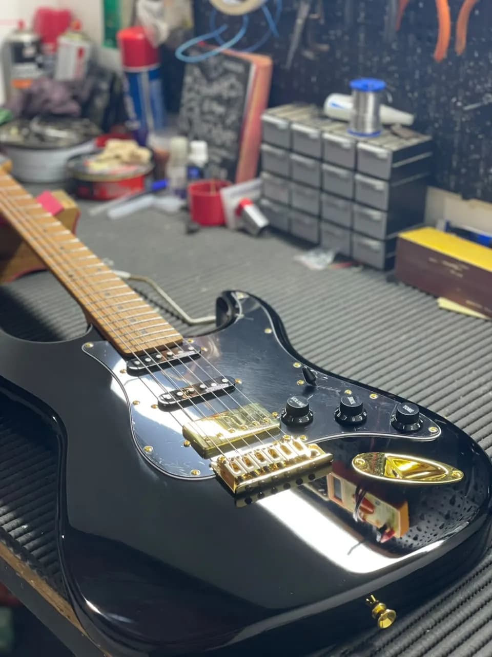 Guitarra stratocaster preta com ferragens douradas recebendo serviço na parte elétrica