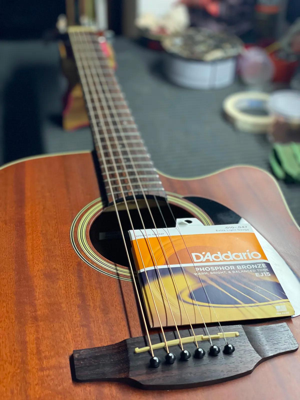 Embalagem de cordas D'Addario Phosphor Bronze sobre violão folk durante a troca de cordas