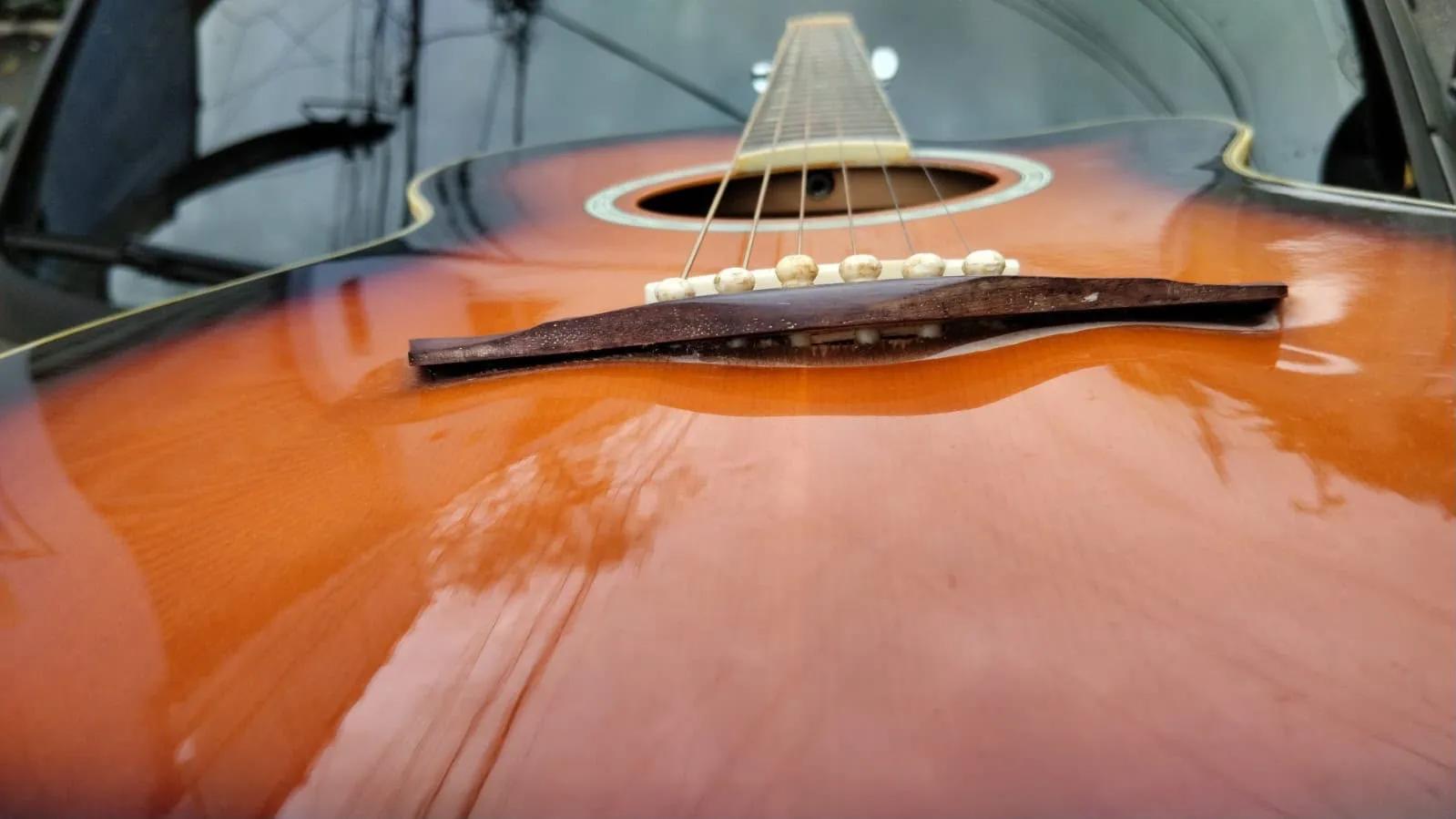 Cavalete descolando do tampo de um violão sunburst, com a folga visível sob a madeira
